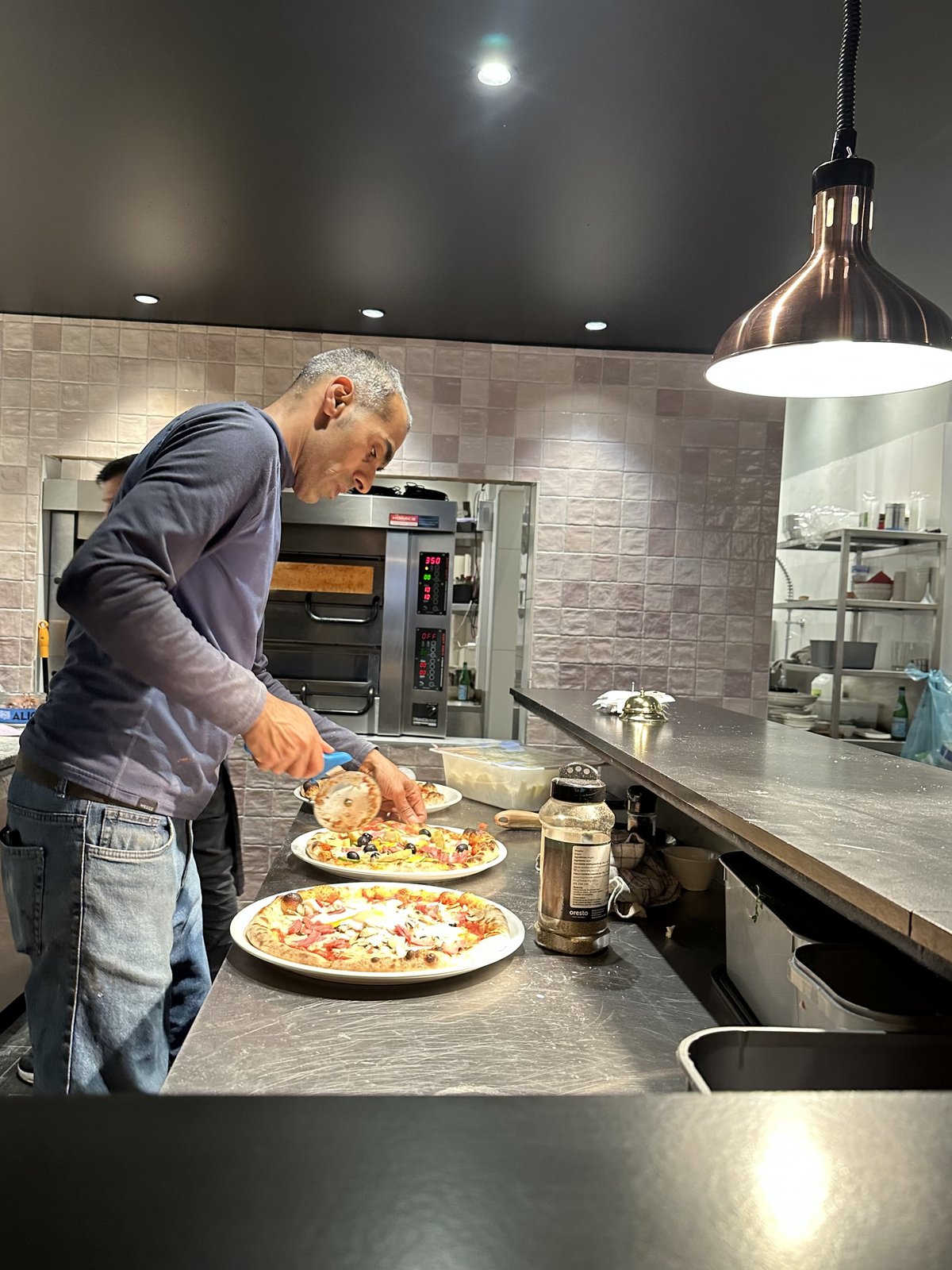 Pizzabakker werkt verse pizza's af in de open keuken